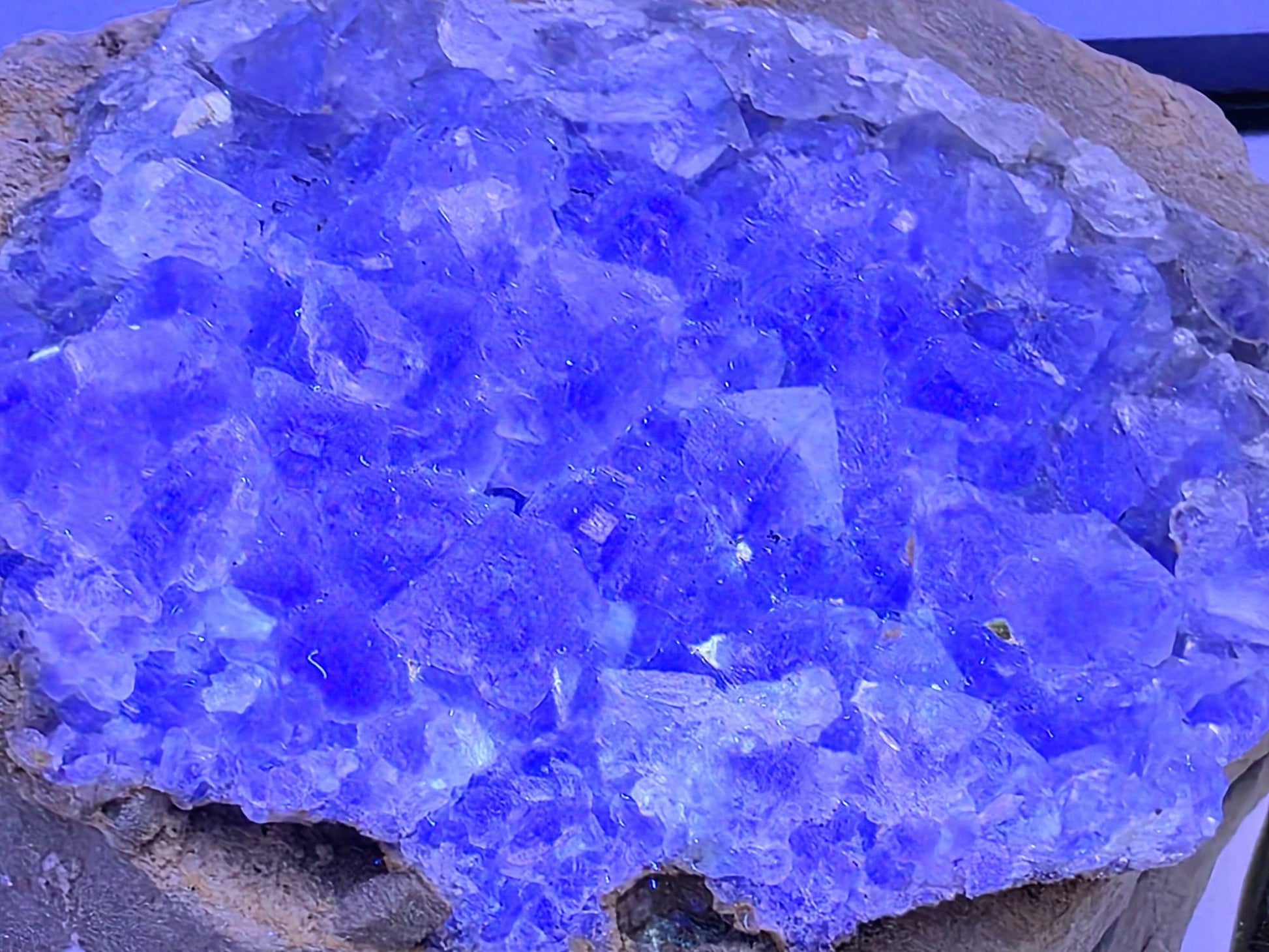 Fluorite crystal glowing with bright blue fluorescence under UV light.