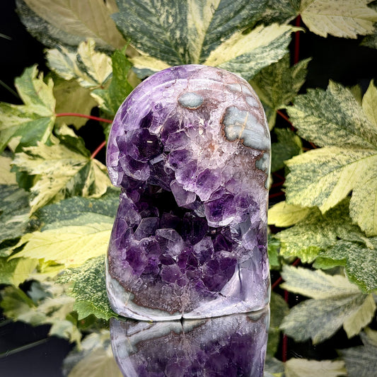 Uruguayan amethyst crystal freeform with purple crystal points and polished face rim displayed on a reflective surface.