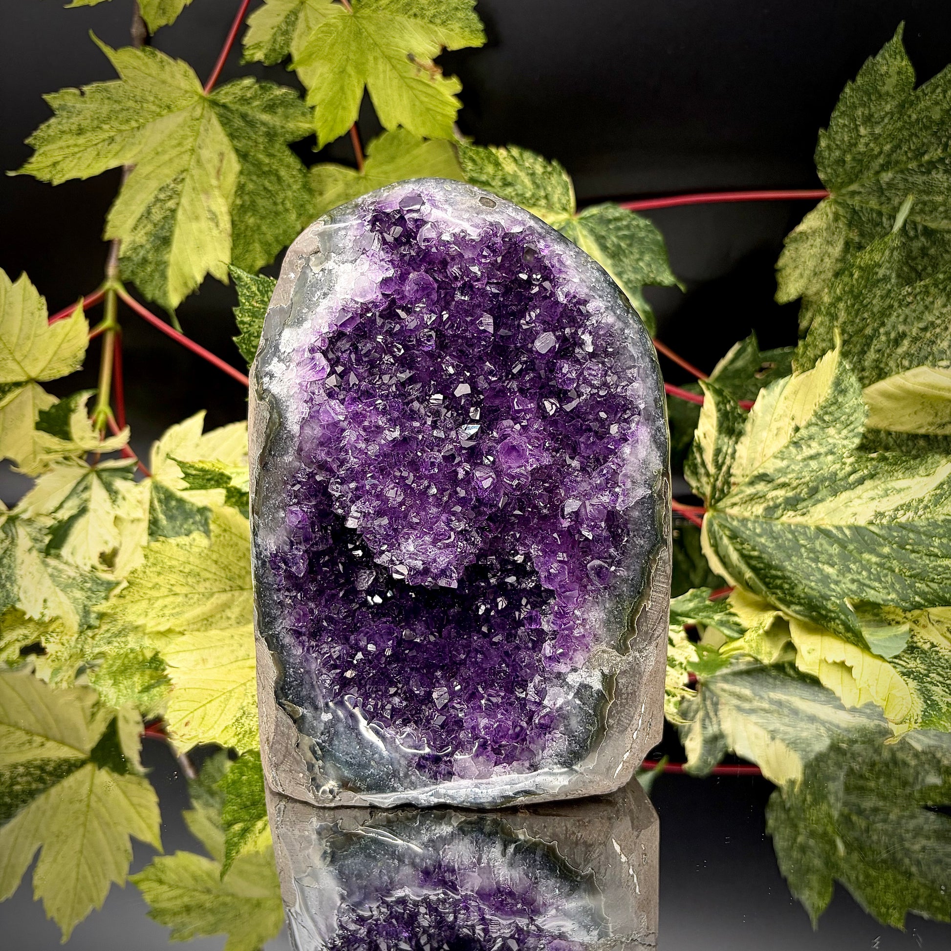 Uruguayan amethyst crystal freeform with purple crystal points and polished face rim displayed on a reflective surface.