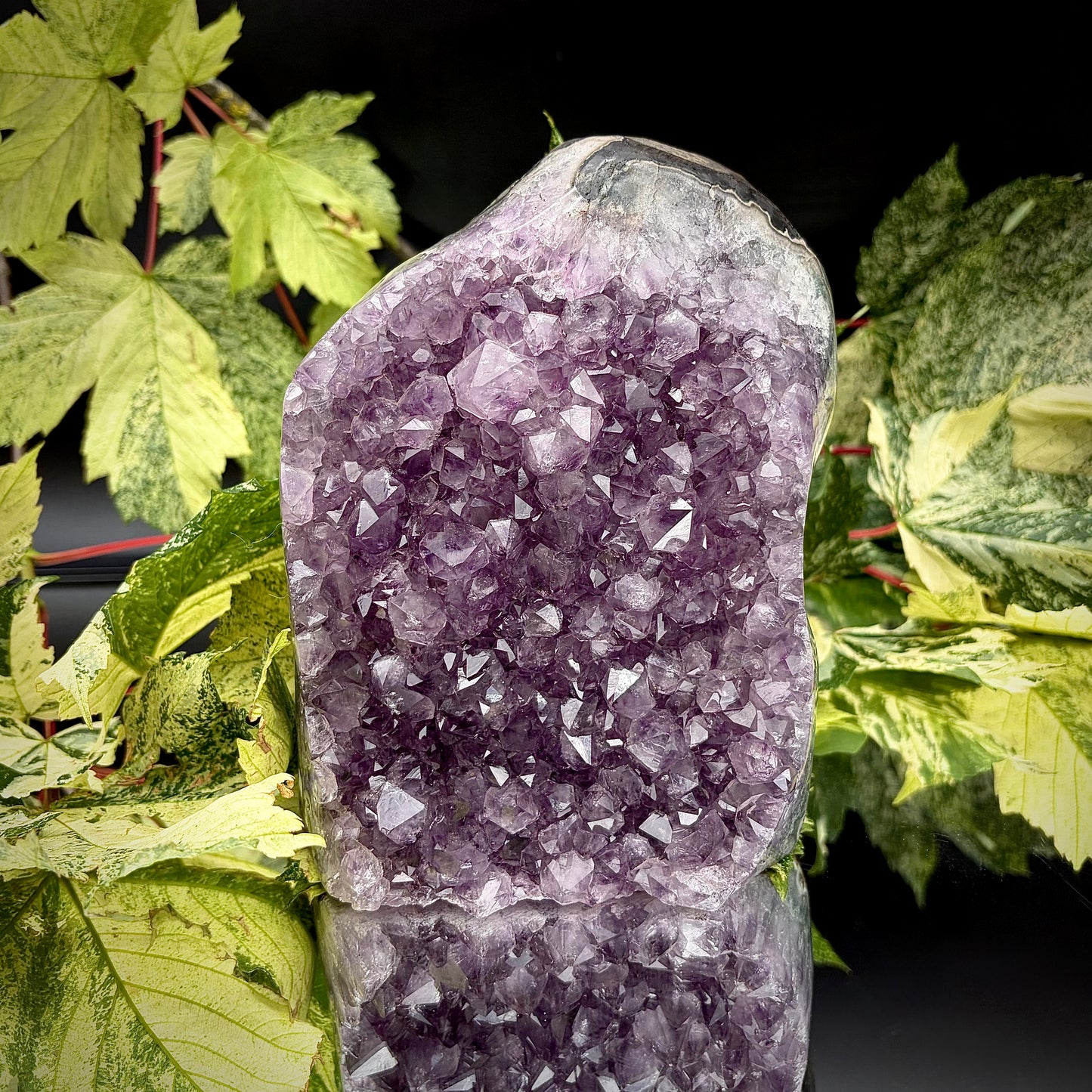 Uruguayan amethyst crystal freeform with purple crystal points and polished face rim displayed on a reflective surface.