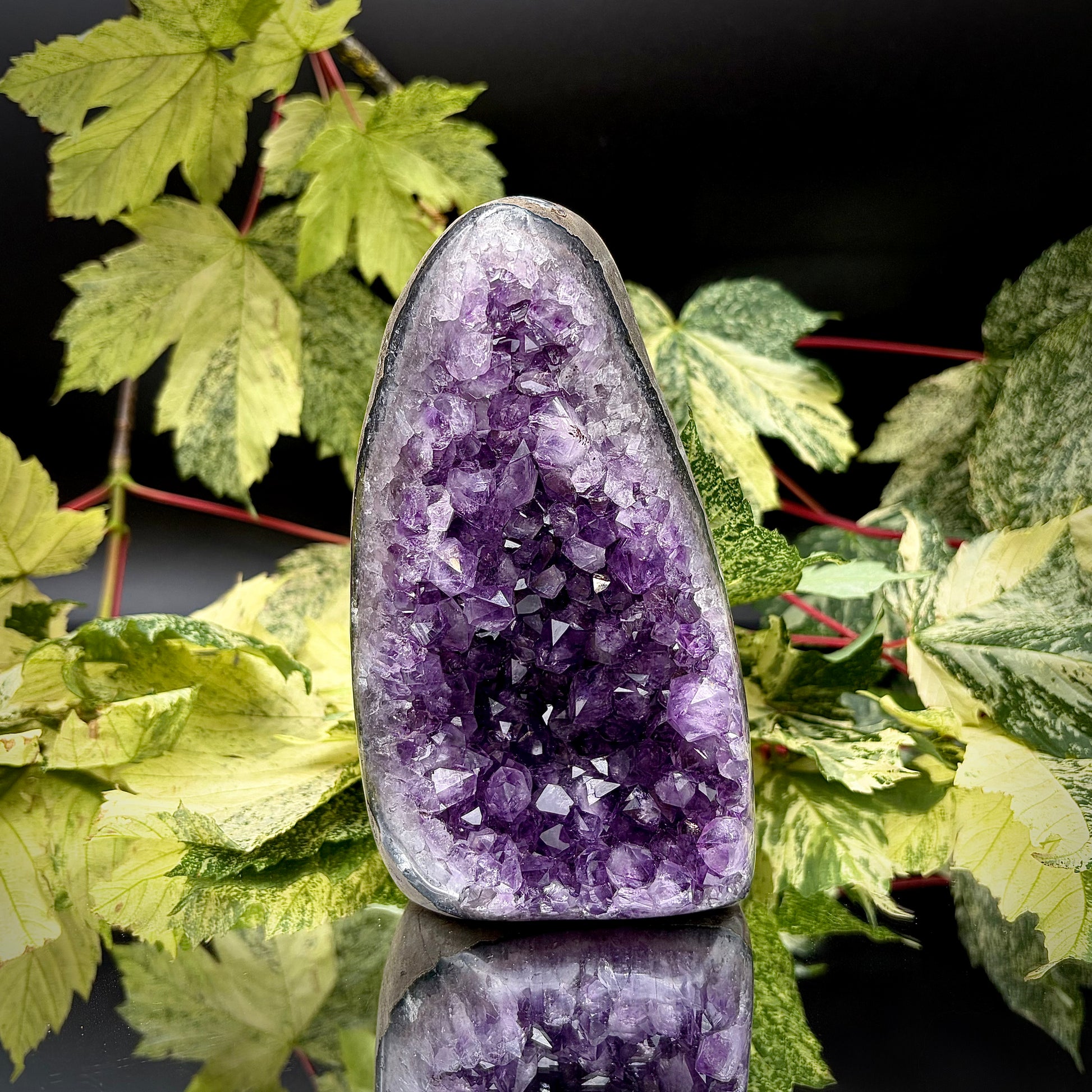 Uruguayan amethyst crystal freeform with purple crystal points and polished face rim displayed on a reflective surface.