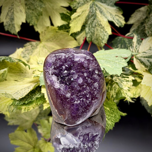 Uruguayan amethyst crystal freeform with purple crystal points and polished face rim displayed on a reflective surface.