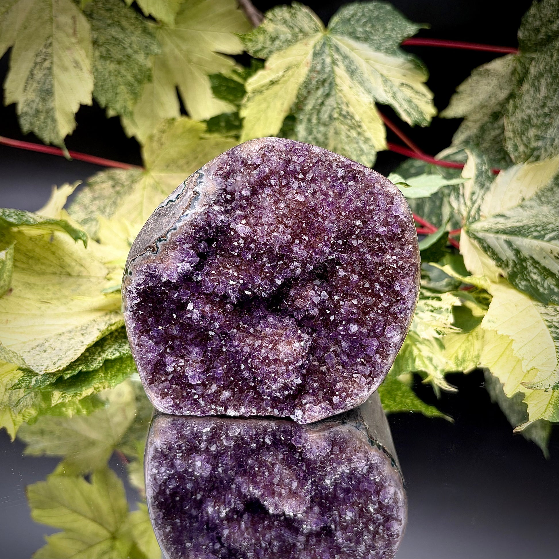 Uruguayan amethyst crystal freeform with purple crystal points and polished face rim displayed on a reflective surface.