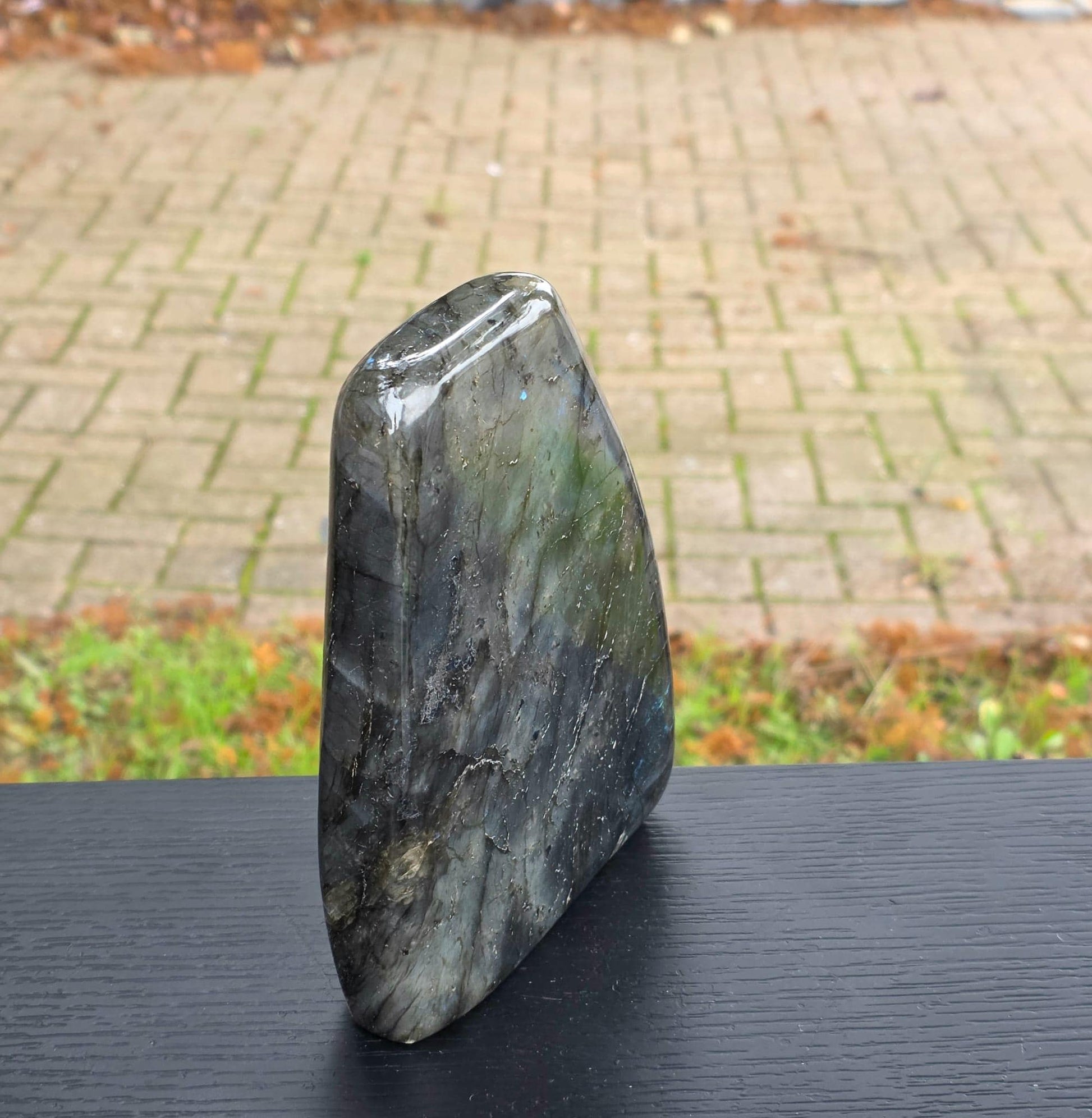 Freeform labradorite specimen with vibrant blue-green iridescence under natural light.