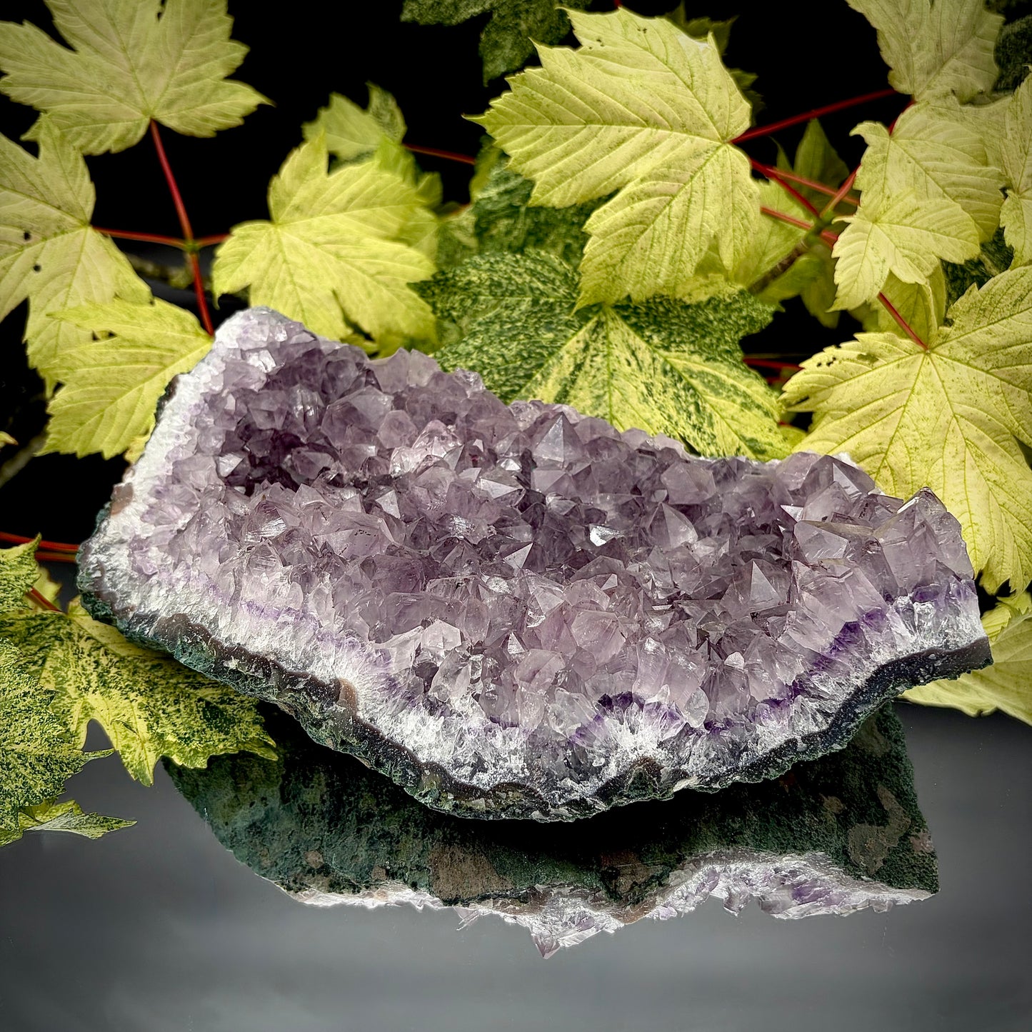 Natural amethyst crystal cluster with purple crystal points displayed on a reflective surface.