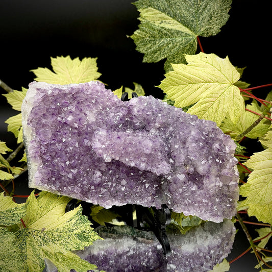 Natural amethyst crystal cluster with purple crystal points displayed on a reflective surface.