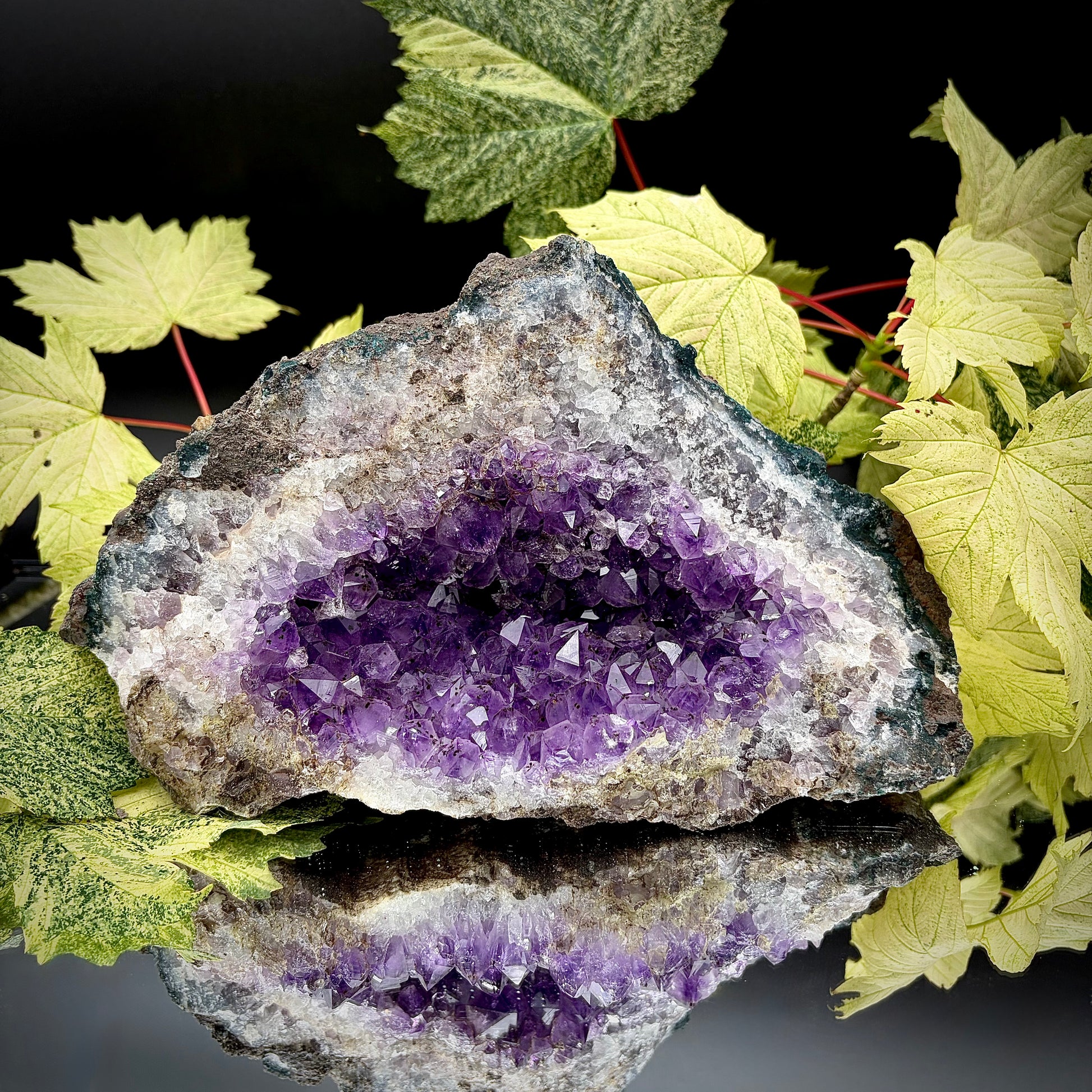 Natural amethyst crystal cluster with purple crystal points displayed on a reflective surface.