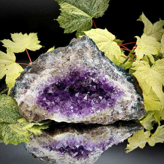 Natural amethyst crystal cluster with purple crystal points displayed on a reflective surface.