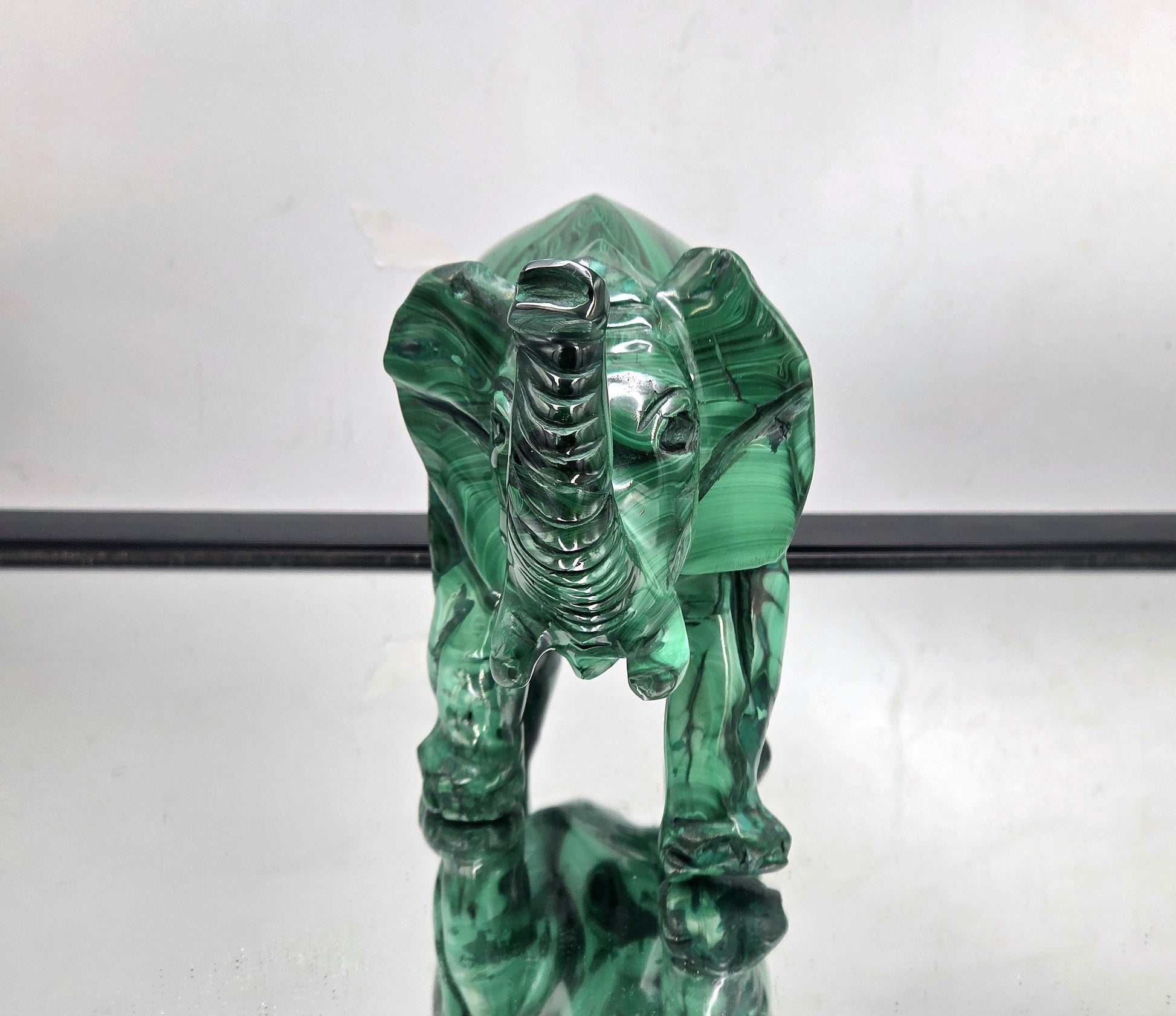 Close-up of a hand-carved malachite crystal elephant showing natural green banding and polished finish.