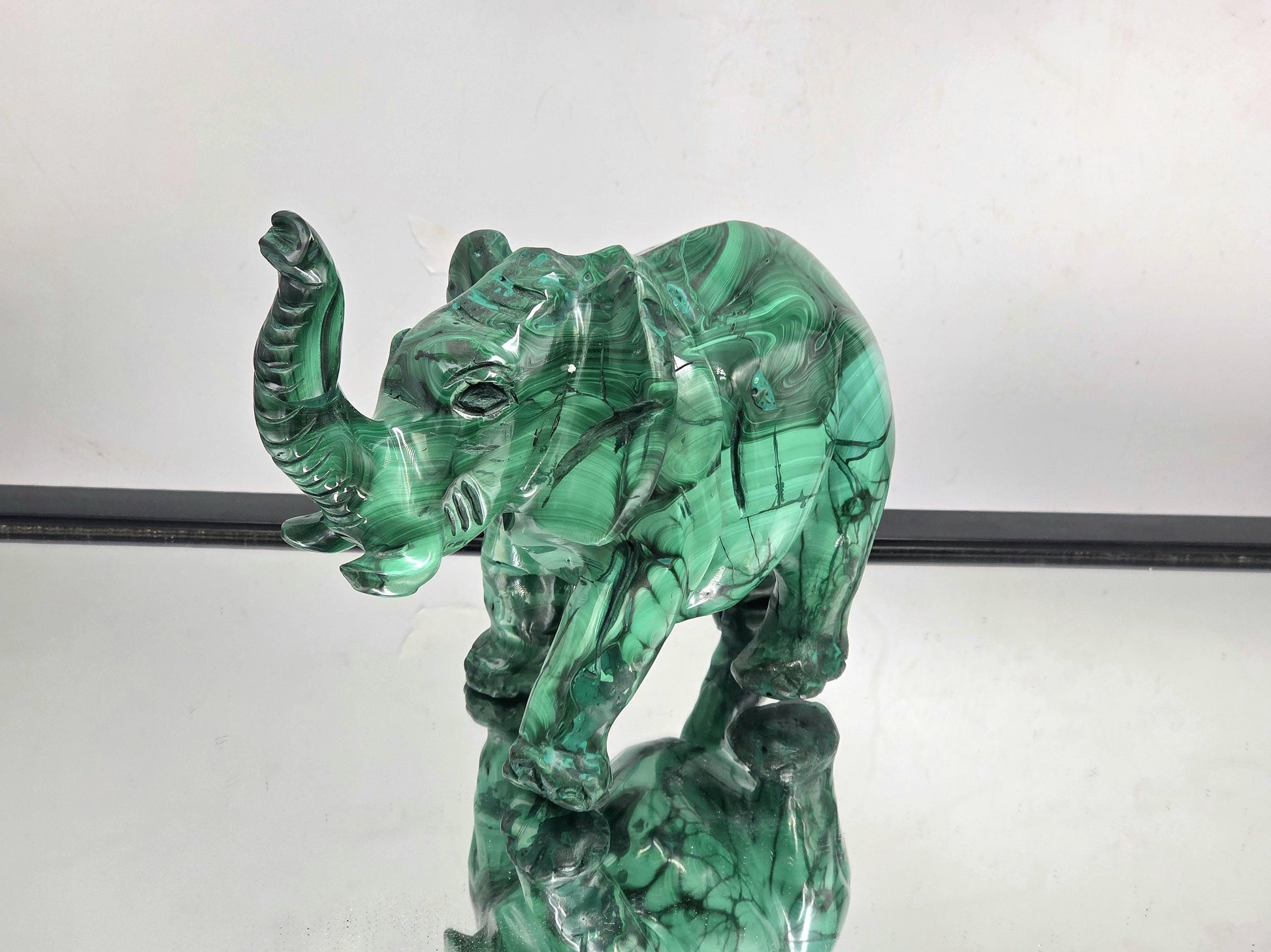 Polished malachite crystal elephant figurine with rich green hues and flowing natural banding patterns.