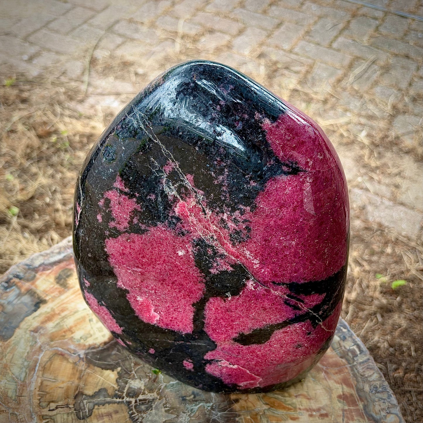A polished free-standing rhodonite crystal sculpture displayed on a wooden stump.