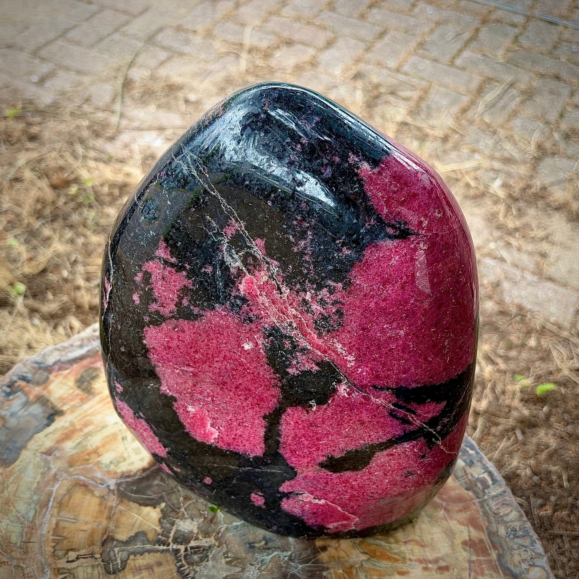 A polished free-standing rhodonite crystal sculpture displayed on a wooden stump.