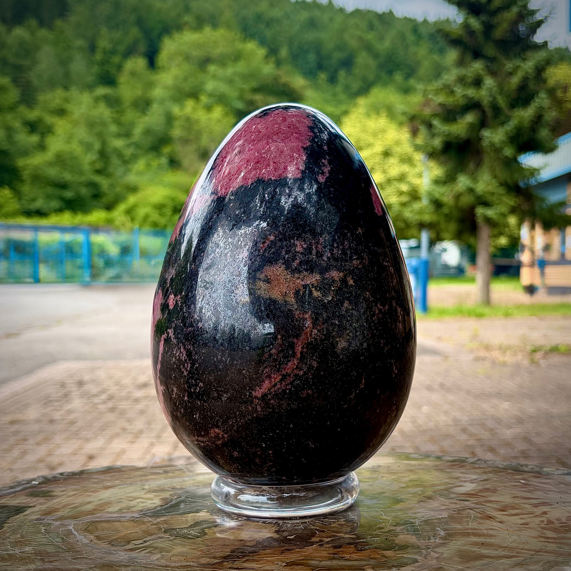The reverse angle of a polished rhodonite crystal egg, displaying a predominantly dark black manganese matrix with a single large pink section near the top apex.
