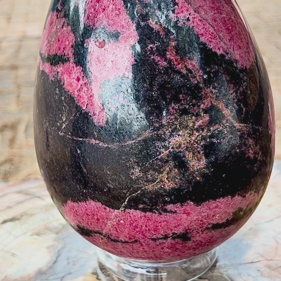 Video showcasing a polished rhodonite crystal egg to reveal its natural pink inclusions and black patterns in daylight.