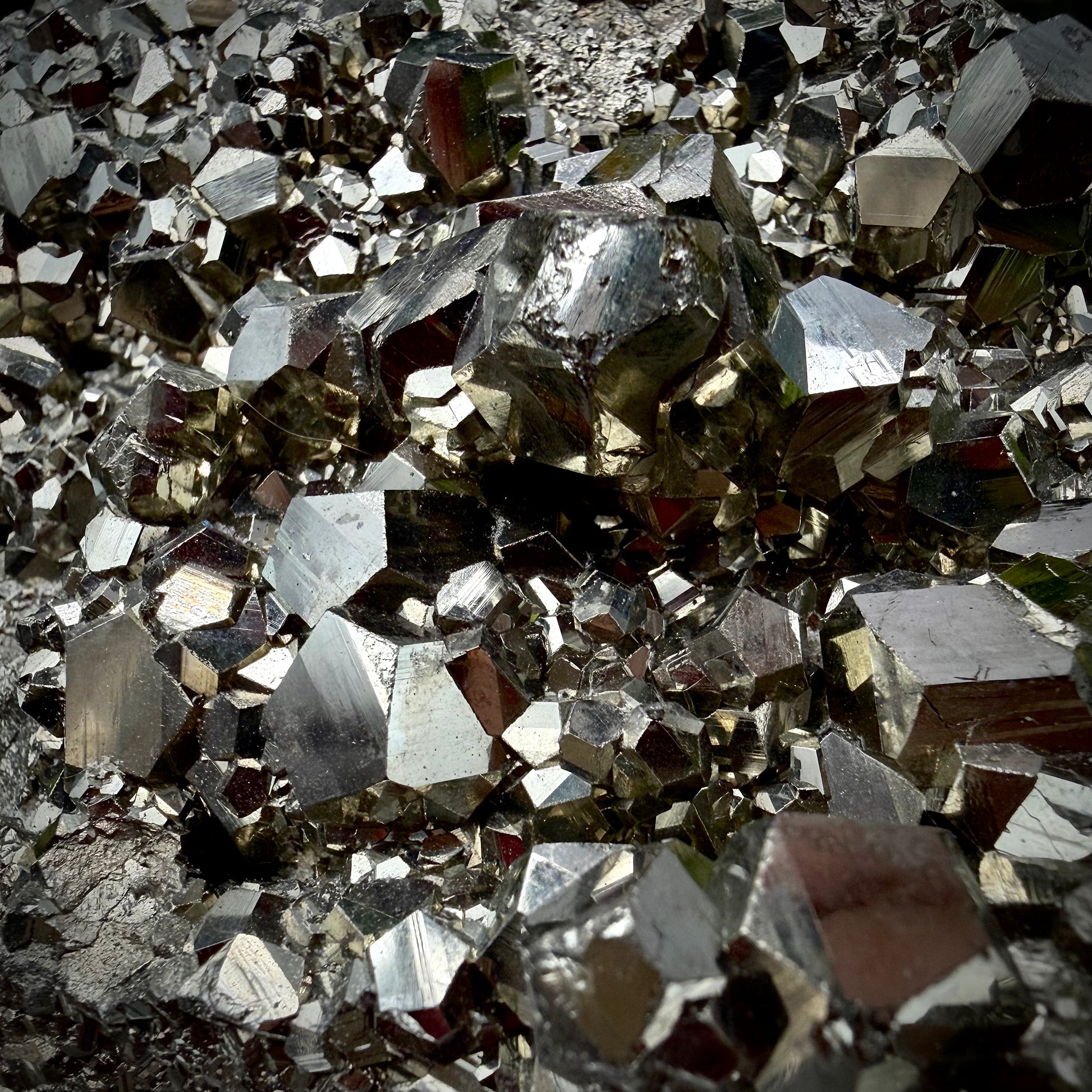 Close-up of multi-faceted geometric pyritohedral crystal formations on a raw Pyrite specimen.