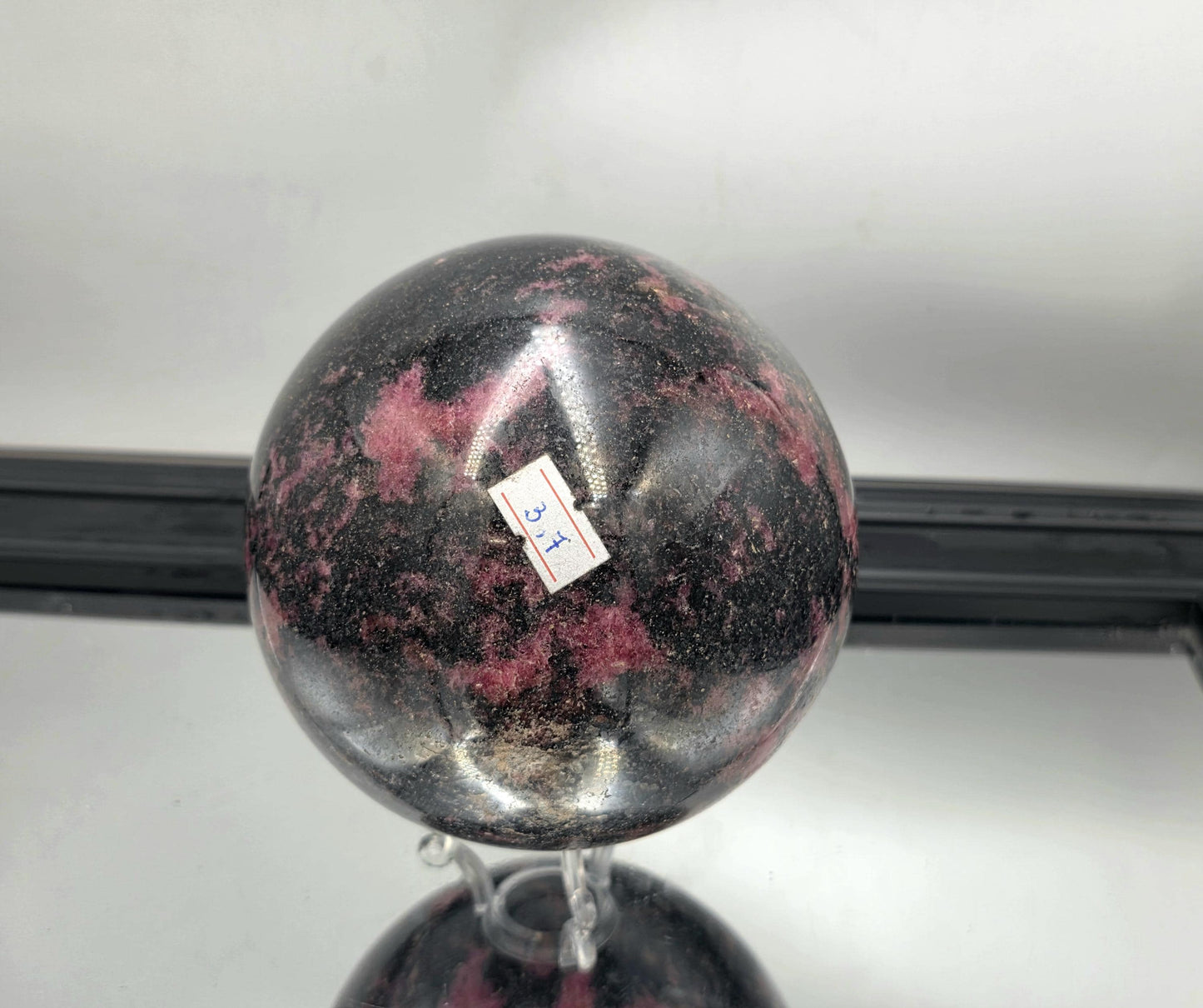 Glossy rhodonite sphere featuring bold organic streaks.